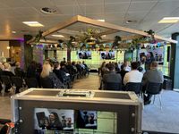 View from the rear of the audience of an event, where the current focus is a live feed on several screens on stage.