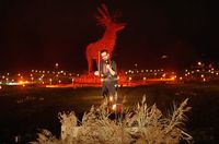 In the foreground, a musician plays a bowed instrument. In the background, a large statue of a stag is lit in deep red.