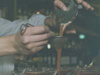 Closeup of a dark brown liquid being poured through a filter into a martini glass.