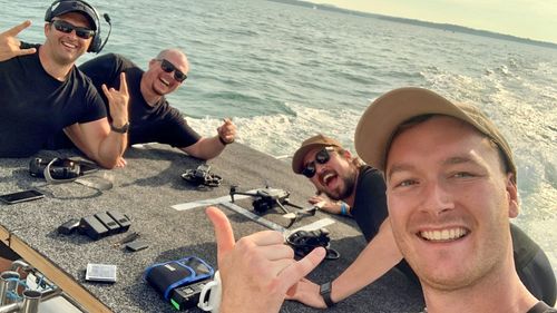 A group of people pose with drones at the rear of a boat.