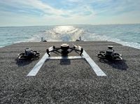 Three drones are on the rear of a boat, with open water in the background.