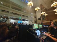 View of an event in a large atrium. In the foreground, two people are operating a control board.